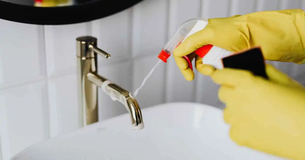 Person cleaning a bathroom sink during a recurring house cleaning visit